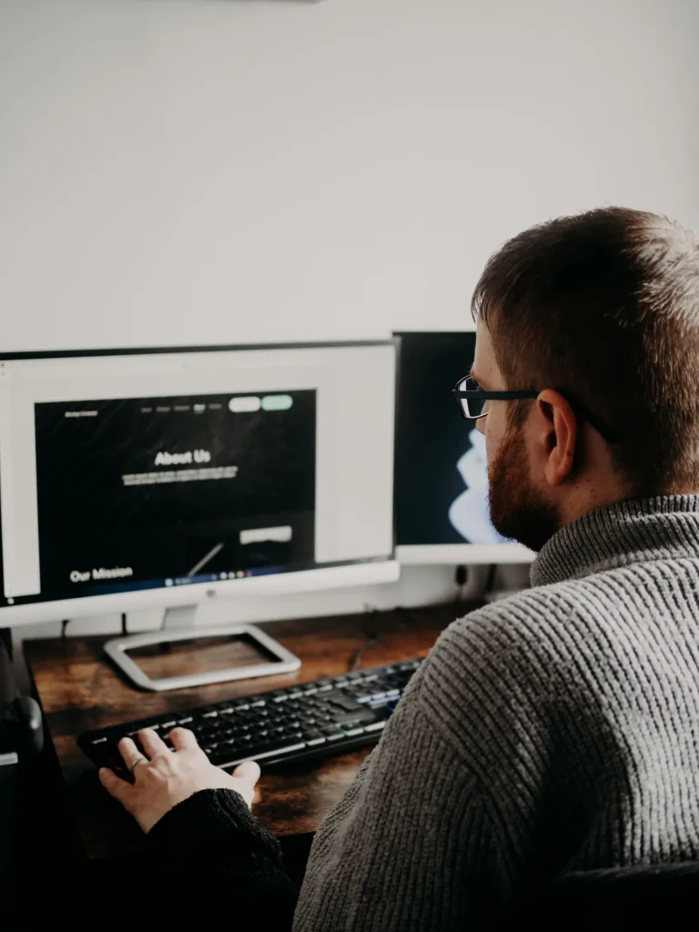 Homem a trabalhar num computador de secretária com dois monitores