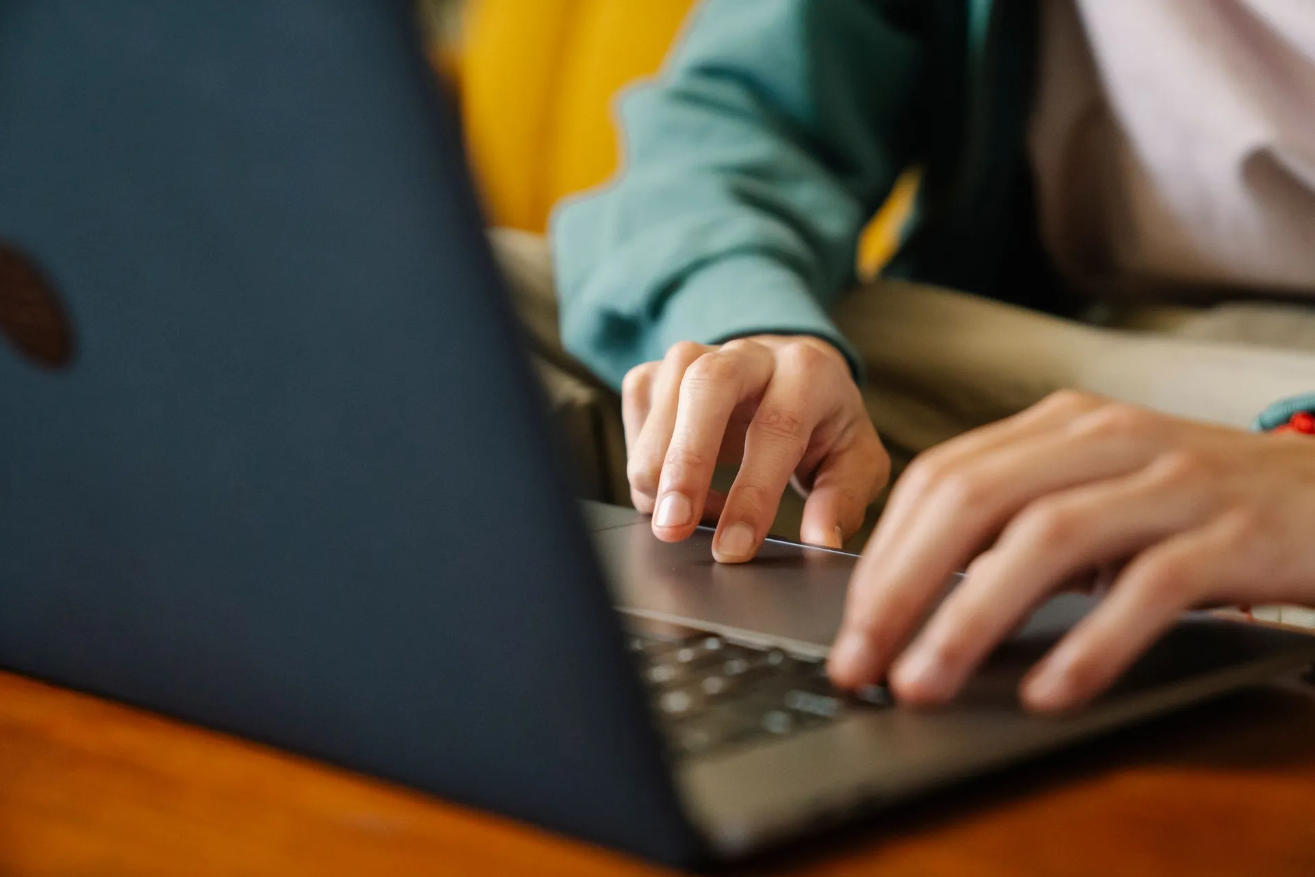 Mãos a escrever no teclado de um portátil aberto numa secretária
